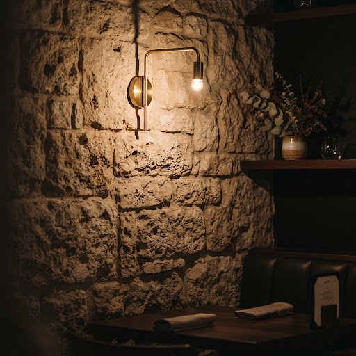 Detail of a textured stone wall bathed in warm light beside a brass light fixture.