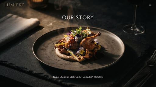 Moody, high-contrast plated fine-dining dish on textured dark stone with rising steam.